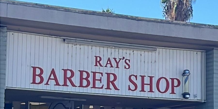 The red RAY'S BARBER SHOP letters and barber pole on the storefront at 12403 Woodside Ave